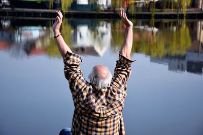 Rear view of man with arms raised sitting by lake