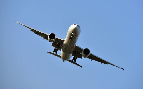 Low angle view of airplane flying against clear blue sky