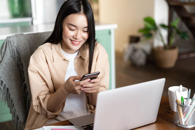 Young woman using mobile phone while sitting at home