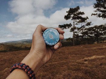 Close-up of hand holding clock against tree