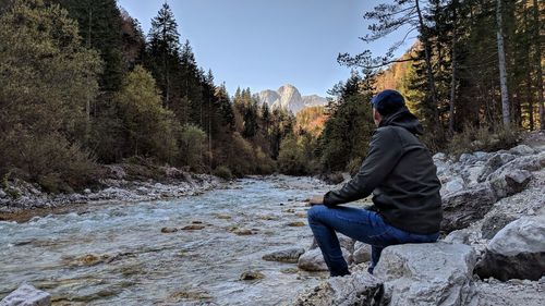 Rear view of man sitting on rock against trees