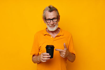 Portrait of senior man holding cup gesturing against yellow background