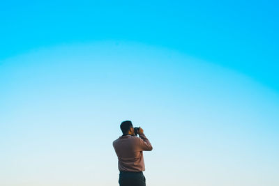 Rear view of man photographing against blue sky