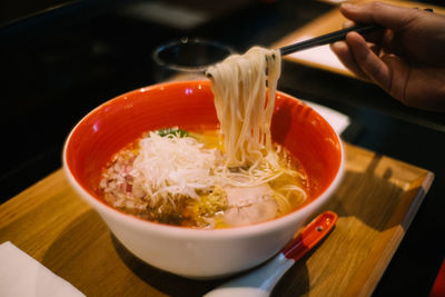 Cropped hand holding noodles in bowl on tray