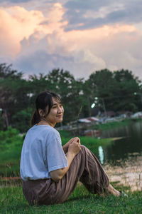 Young woman sitting by lake during sunset