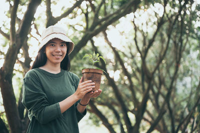 Portrait of smiling young woman standing against tree