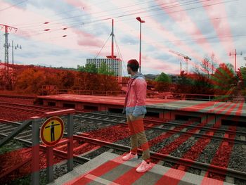 Rear view of woman standing by railroad tracks against sky