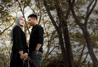 Young couple standing by tree against plants