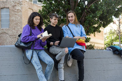 Young diverse people with lgbt rainbow flag using laptop and book outdoors.