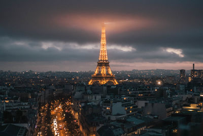 Illuminated buildings in city against cloudy sky