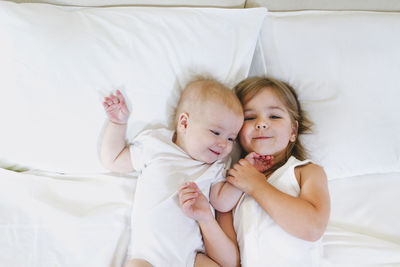 High angle view of siblings lying down on bed at home