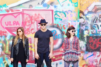 Fashionable people standing against graffiti on wall