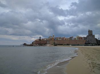 View of city by sea against cloudy sky