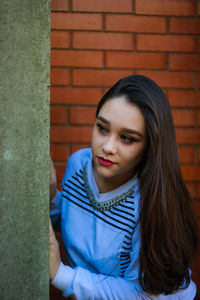 Woman looking away against brick wall