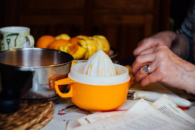 Cropped hands of person by fruits and juicer on table at home
