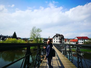 Portrait of woman gesturing peace sign while standing on footbridge over river