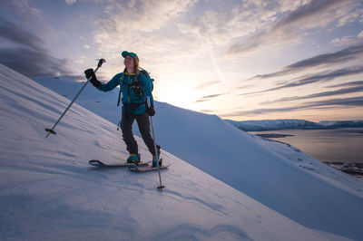 Woman backcountry skiing in iceland at sunrise with water behind