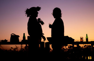 Silhouette people standing against orange sky during sunset