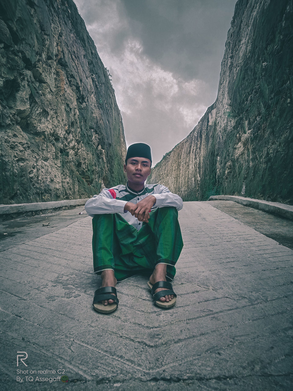 FULL LENGTH PORTRAIT OF YOUNG MAN SITTING ON WALL