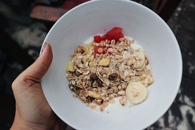 Close-up of hand holding white bowl of cereals 