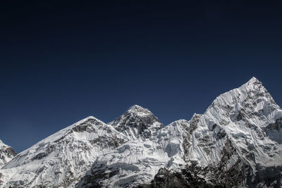 Low angle view of snowcapped mountains against clear blue sky