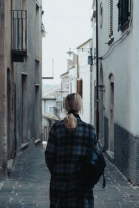 Rear view of woman walking on footpath amidst buildings in city