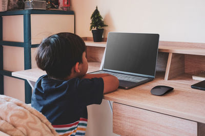 Rear view of boy sitting on table at home