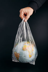 Cropped man holding globe in plastic bag against black background