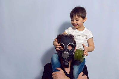 Father and son stand in apartment in a gas mask to protect against coronavirus virus during pandemic