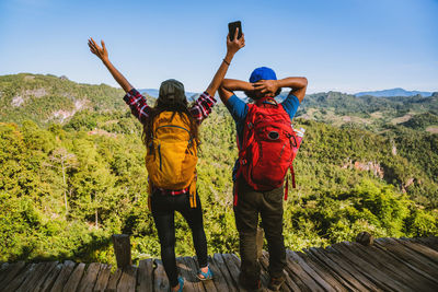 Rear view of men with arms raised on mountain against sky