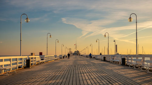 Street leading towards pier against sky during sunset