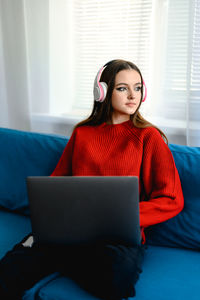 A young girl in a red  sweater works on a laptop at home. her cat and dog are sitting next to her