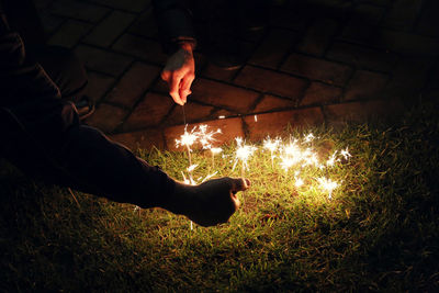 Cropped hand burning sparklers on field at night