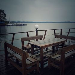 Empty chairs and table by sea against sky