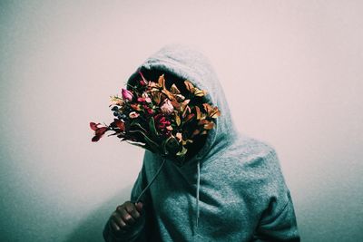 Woman covering face with flowers against wall