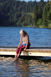 Full length of senior woman sitting on pier by lake