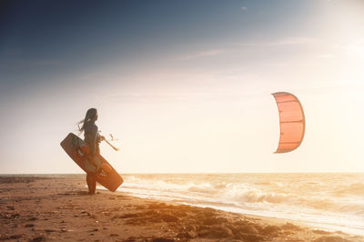 Kiteboarding. kitesurfing athlete woman at sunset stands on the sandy shore holding her kite in the
