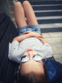High angle view of teenage girl wearing sunglasses while lying on bench