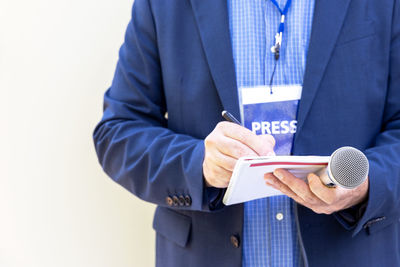 Male reporter with press pass at news conference or media event, holding microphone, writing notes