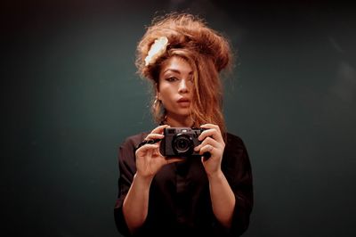 Portrait of young woman with camera against black background