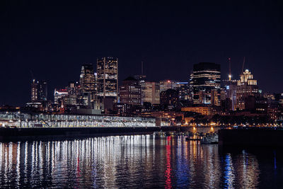 Illuminated buildings by river against sky at night