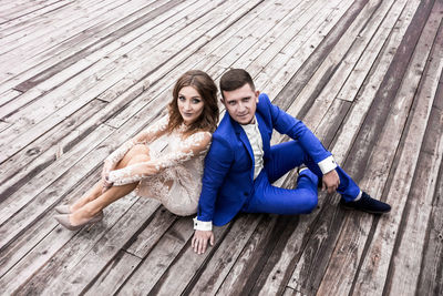 High angle portrait of bride and bridegroom sitting on wooden footpath