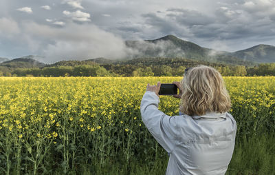 Rear view of woman photographing on field against sky