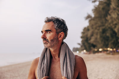 Thoughtful shirtless man with towel on vacation at beach