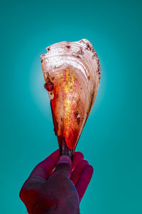 Close-up of hand holding ice cream against blue background