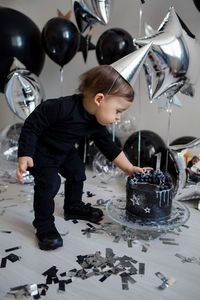 Boy stands next to a festive black cake and balloons