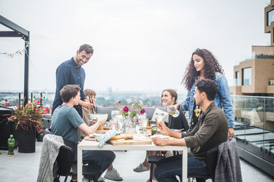 Young male with female serving food and drinks to friends during social gathering on rooftop