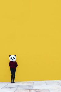 Full length of person standing on footpath against yellow wall