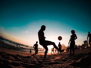 Silhouette people playing on beach against sky during sunset