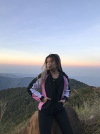 Rear view of woman standing on landscape against sky during sunset